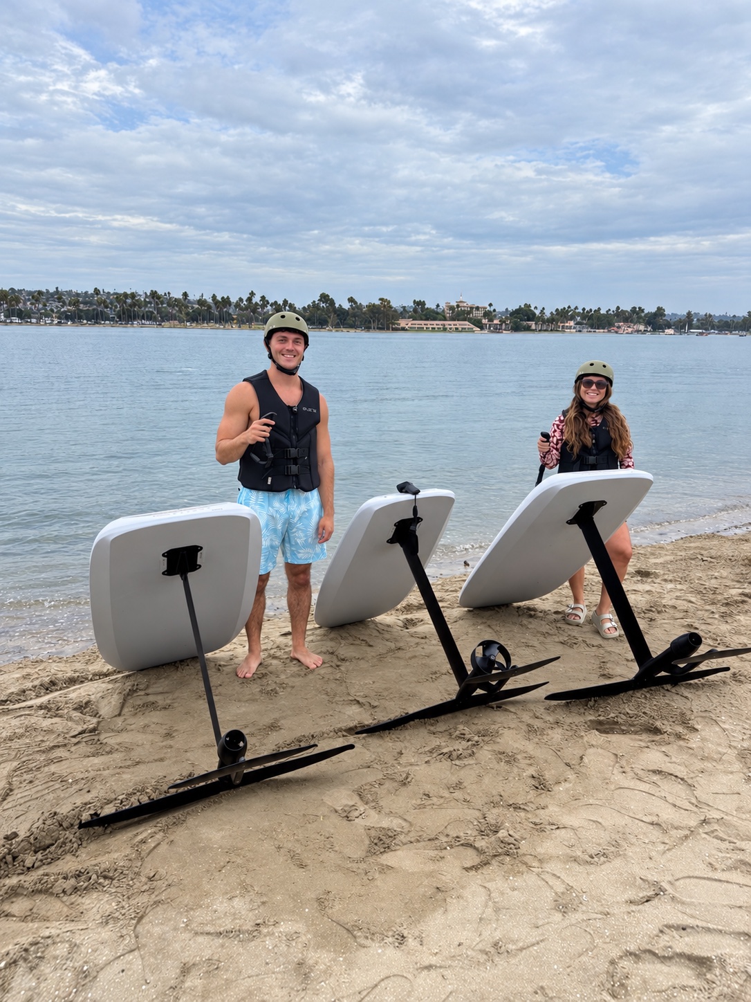 Two smiling riders with their eFoil boards beside the bay