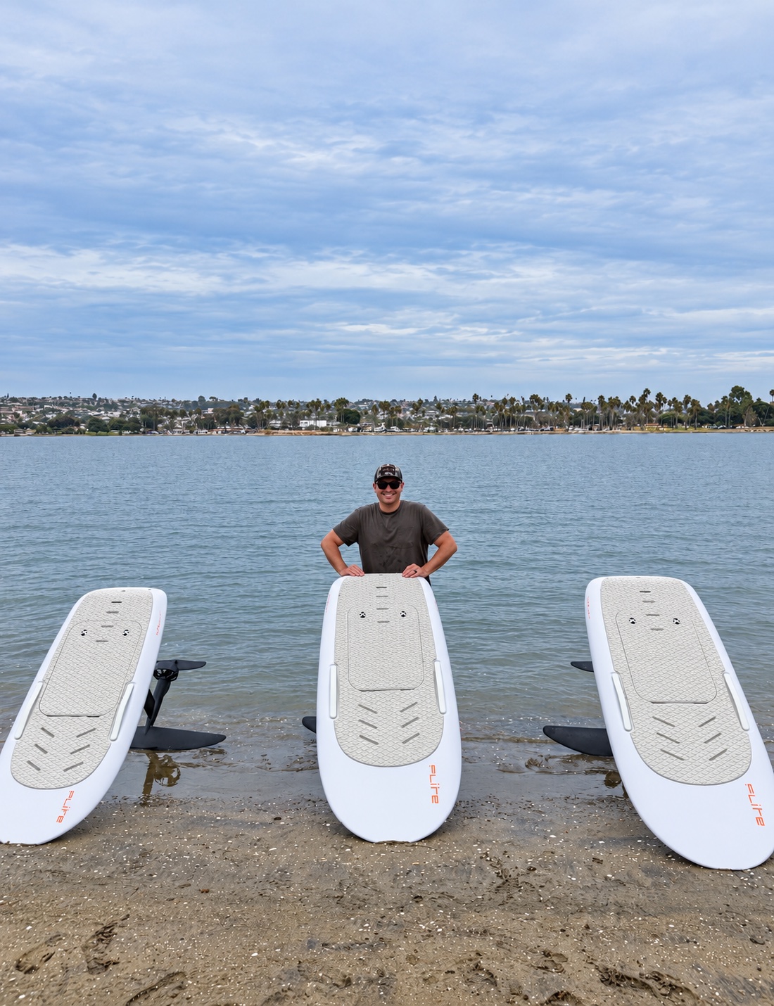 A smiling rider standing behind three eFoil boards at the bay